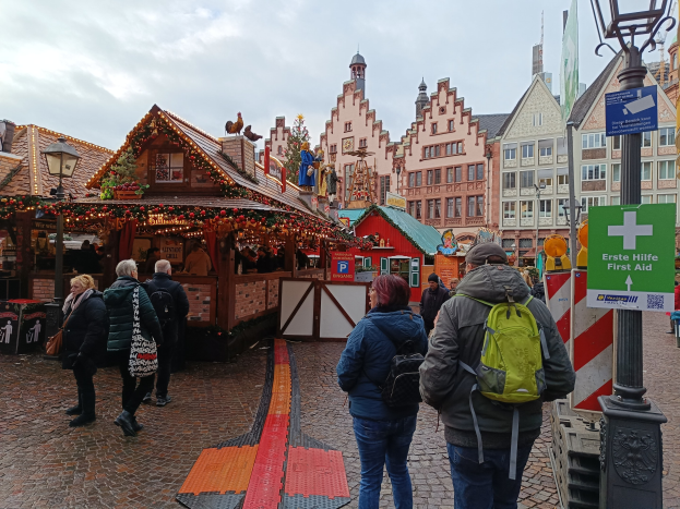 Menschen spazieren auf einem Kopfsteinpflasterweg neben einem Weihnachtsmarkt in Nürnberg, Deutschland, mit Laternenmasten, Texttafeln und Gebäuden im Hintergrund.