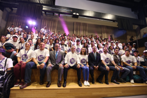 Gruppe von Menschen auf einer Bühne mit einer Person im Rollstuhl links, Vorhänge und Scheinwerfer im Hintergrund bei einer NBA-Frauenbasketball-Konferenz.