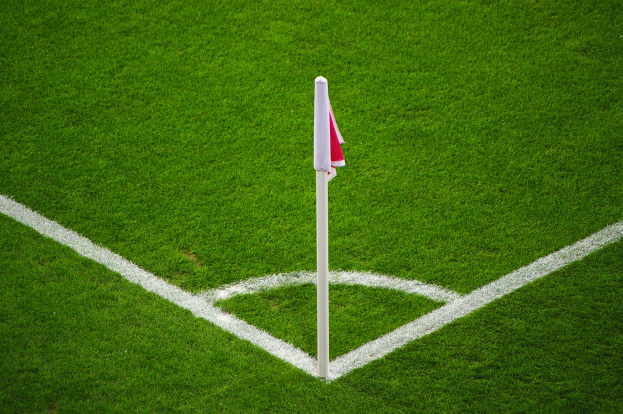 Ein Fußballfeld mit grünem Gras, weißen Begrenzungslinien und einem weißen Pfahl mit einer roten und weißen Flagge auf dem zentralen Elfmeterpunkt.