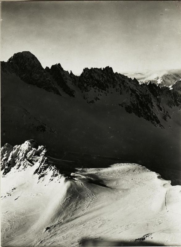 Schwarzes und weißes Foto einer schneebedeckten Gebirgskette mit dem Himmel im Hintergrund, unten mit "Albert Bierstadt - Die Alpen" beschriftet.