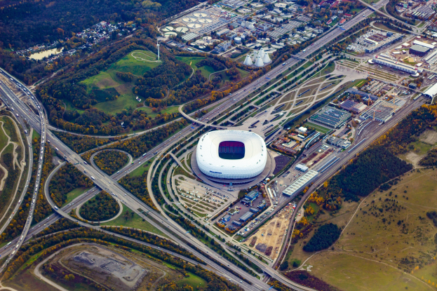Luftaufnahme des Olympiastadions in München, Deutschland, umgeben von Gebäuden, Bäumen, Straßen, Fahrzeugen und Gras.