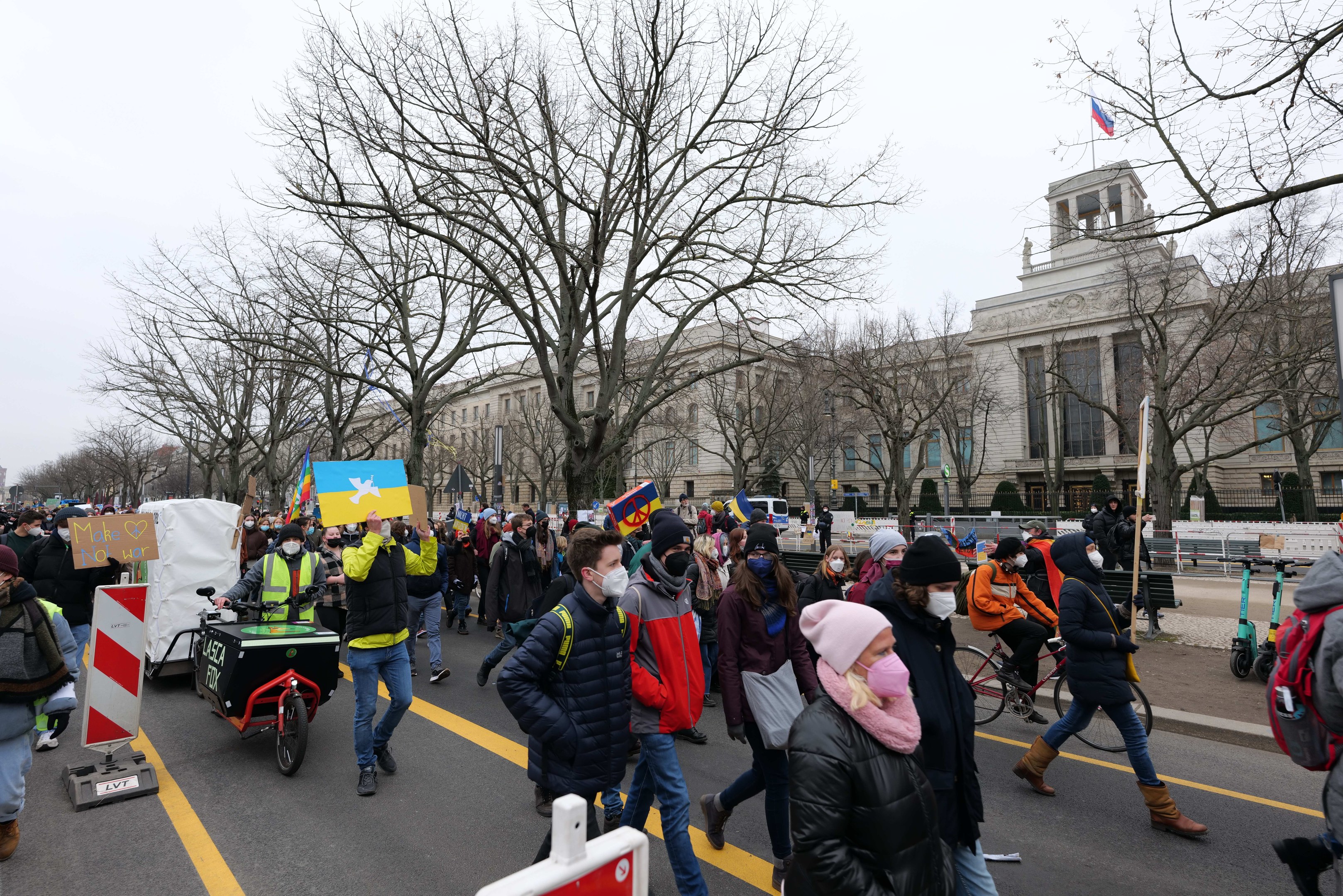 Eine große Gruppe von Menschen marschiert bei einer Demonstration in Washington, D.C. am 21. Januar 2020 mit Schildern, Fahrrädern, Bäumen, Schilderständern und einem Gebäude im Hintergrund unter einem klaren blauen Himmel.