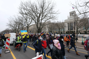 Eine große Gruppe von Menschen marschiert bei einer Demonstration in Washington, D.C. am 21. Januar 2020 mit Schildern, Fahrrädern, Bäumen, Schilderständern und einem Gebäude im Hintergrund unter einem klaren blauen Himmel.