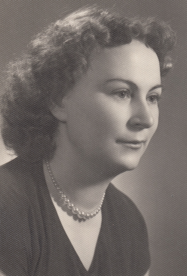 Ein Schwarz-Weiß-Foto einer Frau mit ernstem Gesichtsausdruck, die eine Kette trägt und ein einfaches Kleid mit hohem Kragen und langen Ärmeln trägt, mit zurückgebundenem Haar und konzentriertem Blick.