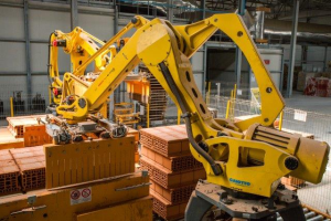 Ein großes Lagerhaus voller Numerous boxes, Kräne, ein Zaun, Pfosten und andere industrielle Ausrüstung, mit einer Wand im Hintergrund.