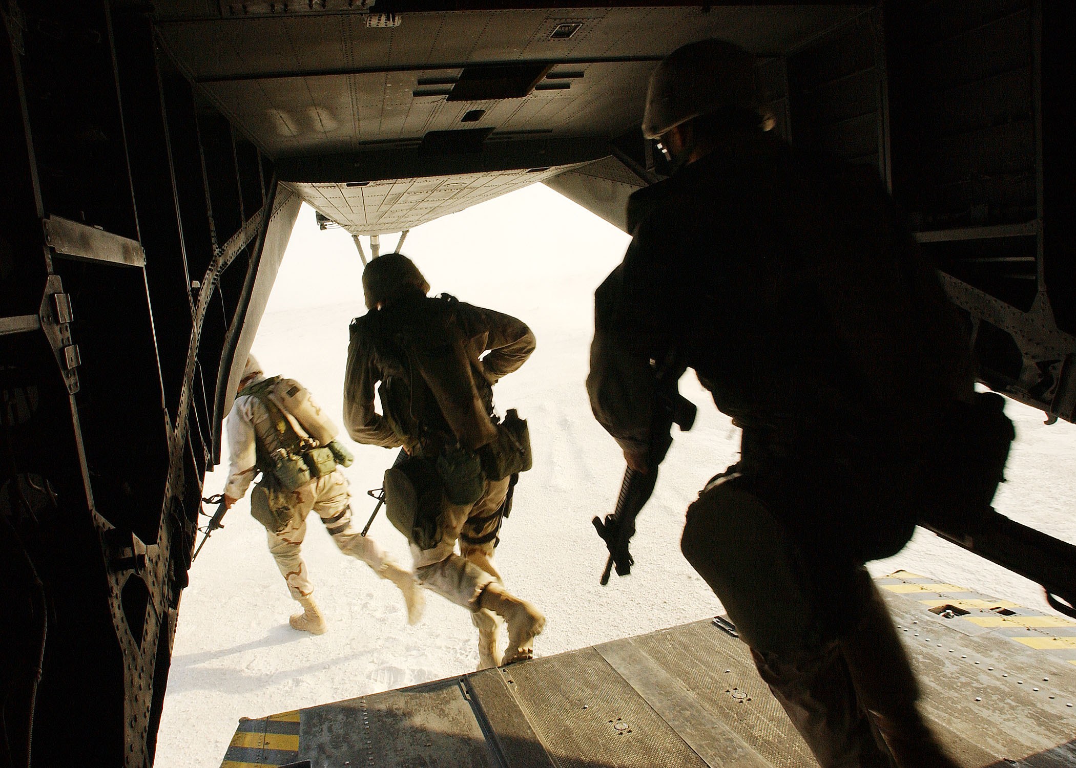 Soldaten in Uniform und Helmen laufen aus einem Flugzeug, jeder trägt ein Gewehr bei sich.