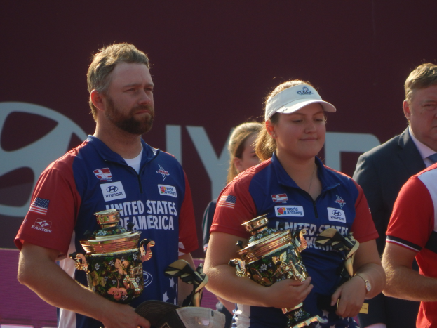 Eine Gruppe von Menschen, die Pokale halten, mit einem "World Archery Championships"-Schild im Hintergrund.