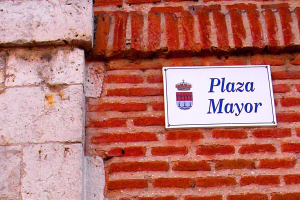 Eine Ziegelwand mit einem rechteckigen Schild, auf dem in fetter, schwarzer Schrift in der Mitte "Plaza Mayor" steht.
