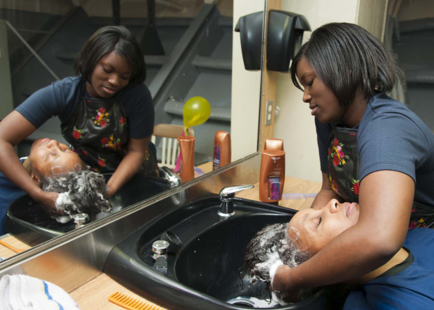 Eine Frau sitzt in einem Salonwaschbecken und erhält eine Haarwäsche, umgeben von Salonartikeln mit Stufen und einer Wand im Hintergrund.