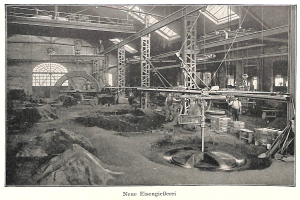 Schwarzes und weißes Foto einer Fabrik mit Arbeitern, die Maschinen bedienen, umgeben von Metallstangen und Polen, mit der Beschriftung "Neue Eisengießerei, die erste Fabrik in Deutschland" unten.