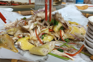 Ein Tisch mit Tellern voller Essen, Schalen mit Sauce, Stäbchen, Gläsern, Flaschen und anderen Essensutensilien in einem Restaurant- oder Bar-Setting, mit einer Person im Hintergrund.