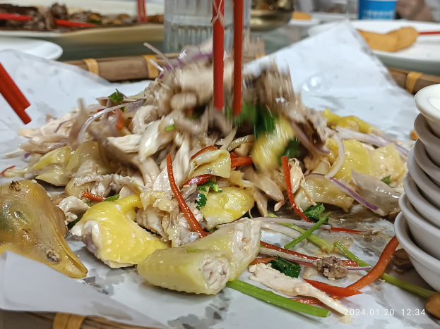 Ein Tisch mit Tellern voller Essen, Schalen mit Sauce, Stäbchen, Gläsern, Flaschen und anderen Essensutensilien in einem Restaurant- oder Bar-Setting, mit einer Person im Hintergrund.