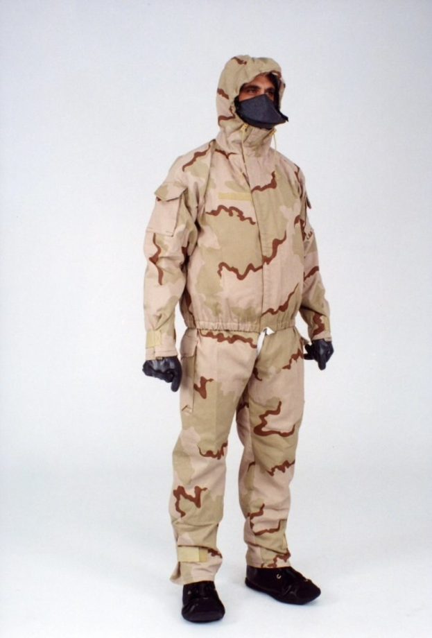 Eine Person in einem camouflagegemusterten Schutzoverall mit Kapuze und Maske steht vor einem weißen Hintergrund.