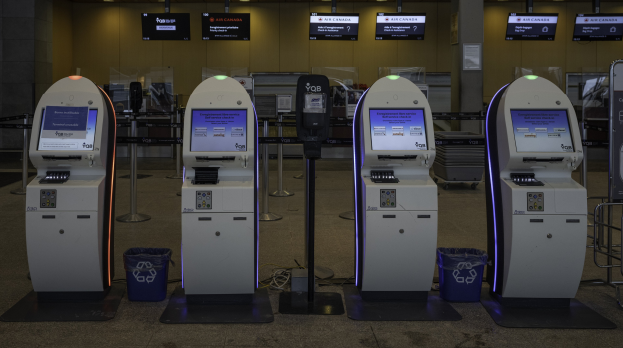 Eine Reihe von Geldautomaten auf einem gefliesten Boden mit Mülltonnen, Pfählen, bedruckten Platten, Lampen und anderen Gegenständen im Hintergrund.