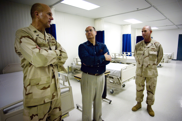 Drei Männer in Militäruniformen in einem Krankenhauszimmer mit Betten, Vorhängen, einer Tür und Deckenleuchten.