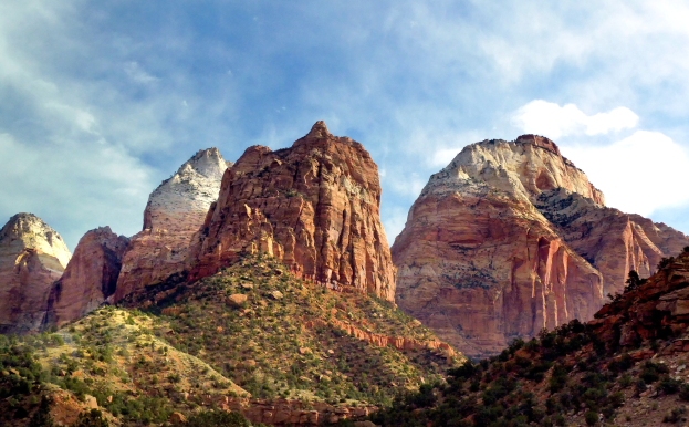 Eine malerische Aussicht auf den Zion-Nationalpark in Utah mit majestätischen Bergen, grünen Bäumen, steinigem Gelände und einem Himmel voller weißer Wolken.