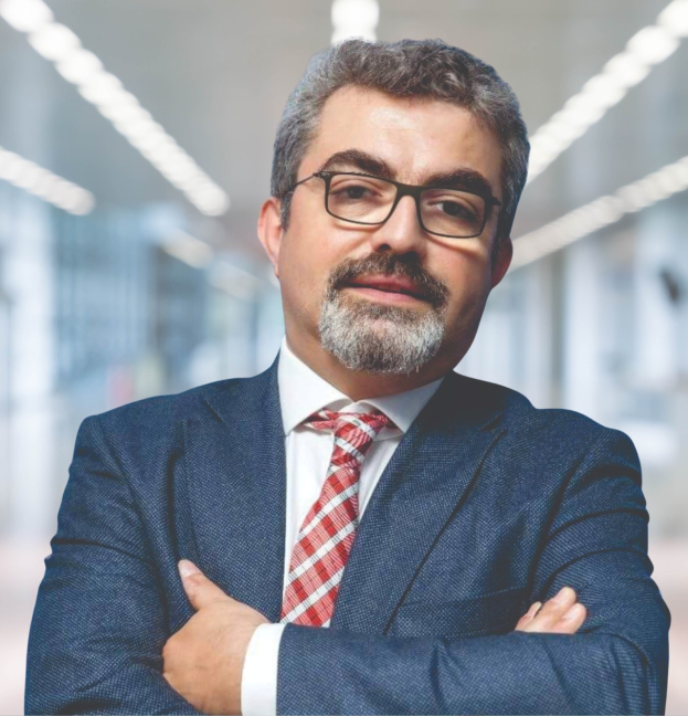 Ein Mann im Anzug und mit Krawatte, der die Arme verschränkt und eine Brille trägt, vor einem unscharfen Hintergrund posiert, identifiziert als der neu ernannte Marketingchef.