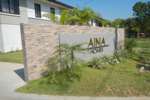 Ein Gebäude mit Fenstern, einem Namensschild, Pflanzen, Gras, einem Weg, Bäumen, Polen, Drähten und einem bewölkten Himmel, das ein zum Verkauf stehendes Grundstück in Imus, Cavite, Philippinen darstellt.