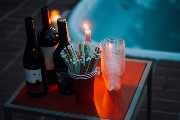 Ein Tisch am Swimmingpool mit zwei Weinflaschen, einer Kerze, Gläsern und Strohhalmen deutet auf einen nächtlichen Pool-Drink hin.