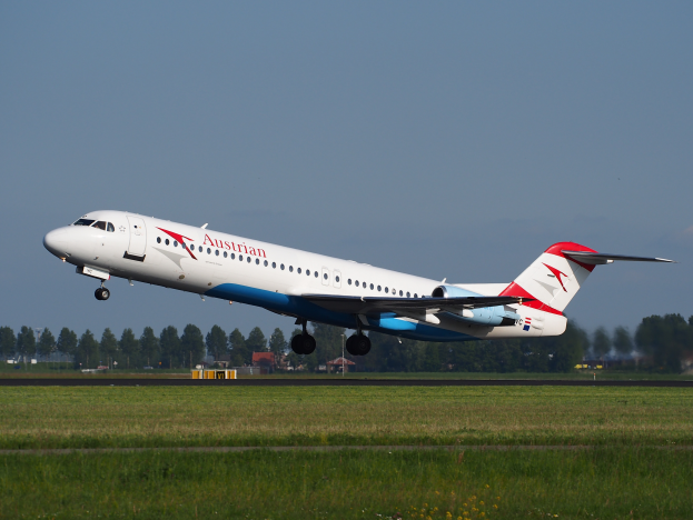 Ein Embraer ERJ-190-Flugzeug der Austrian Airlines beim Start am Frankfurt Airport, mit grünem Gras darunter und Bäumen und Gebäuden im Hintergrund, unter einem klaren Himmel.