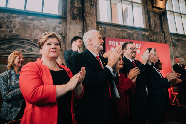 Eine Gruppe von Menschen, die vor einer Menge jubeln, mit einem Banner mit der Aufschrift "Wahlsieg" im Hintergrund.