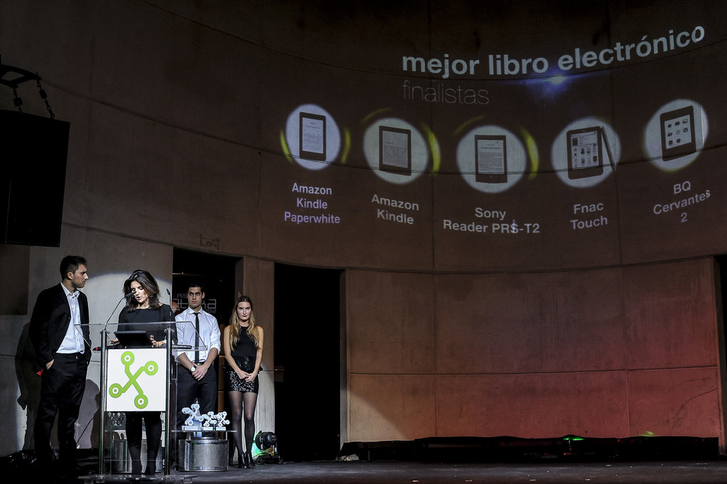 Vier Personen auf der linken Seite, wobei eine Frau einen Vortrag hält; im Hintergrund werden Bilder von Geräten mit ihren Namen darunter angezeigt.