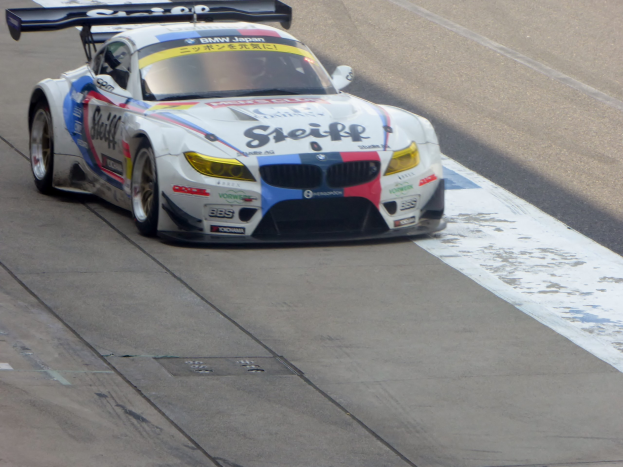 Ein strahlend blauer und weißer BMW Z4 GT3 Rennwagen mit niedrigem Profil, aerodynamischem Design und glänzenden Rädern, der auf einer Rennstrecke fährt.