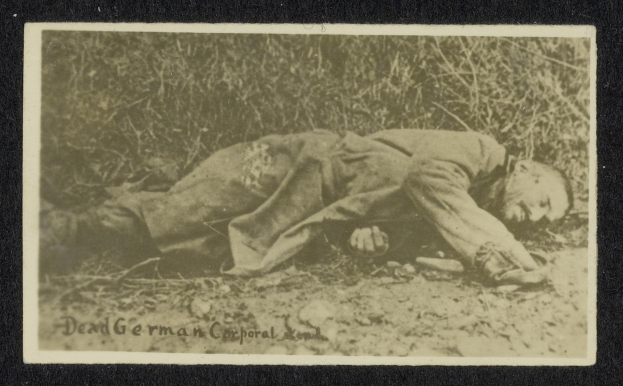 Altes Schwarz-Weiß-Foto eines toten deutschen Korporals, der auf dem Boden liegt und von Pflanzen umgeben ist, mit Text unten.