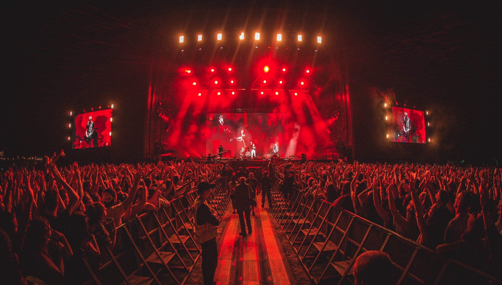 Eine große Menschenmenge steht vor einer hell erleuchteten Bühne mit Musikern, die spielen, und anderen, die zuschauen, vor einem dunklen Hintergrund.