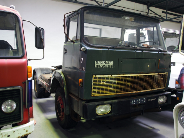 Eine Gruppe von Lkw, die nebeneinander in einer Garage geparkt sind, mit einer Wand und Metallstangen im Hintergrund, darunter einer, die als Frachtlinie gekennzeichnet ist.