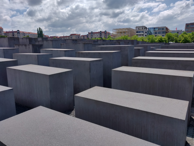 Luftaufnahme des Holocaust-Mahnmals für die ermordeten Juden Europas in Berlin, mit einem Gittermuster aus Betonsteinen und Bäumen und Gebäuden im Hintergrund.