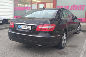 Schwarzer Mercedes-Benz E-Klasse E250 CDI BlueEfficiency Avantgarde Sedan auf einer Straße mit einem Gebäude im Hintergrund, das Glasdoors und Text an der Wand aufweist.