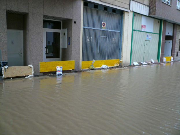 Eine überflutete Straße mit Wasser bis zum Fenster- und Türiveau, das die Umgebung und nahe Objekte überschwemmt.