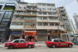 Ein rotes Taxi fährt auf einer von Hochhäusern gesäumten Straße, mit Passanten, Schaufenstern und anderen städtischen Details im Hintergrund, unter einem bewölkten Himmel.