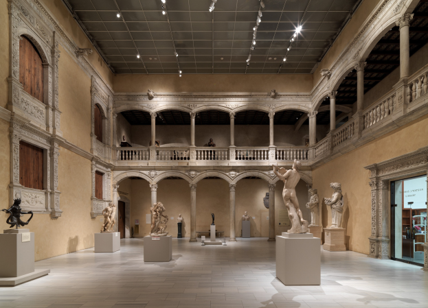 Große Museumsgalerie mit zahlreichen Statuen und Skulpturen auf Sockeln, architektonischen Elementen wie Wänden, Säulen, Geländern und einer beleuchteten Decke sowie einigen Besuchern.