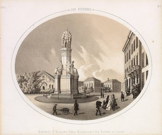 Schwarze und weiße Zeichnung einer Statue des Heiligen Majestrat König Maximilian I. von Bayern in einem Stadtplatz, umgeben von Gebäuden, Bäumen und Menschen, mit Text unten und sichtbarem Himmel im Hintergrund.