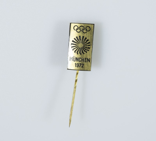 Goldene Nadel mit "München 1972 Olympische Spiele" Text auf weißem Hintergrund.