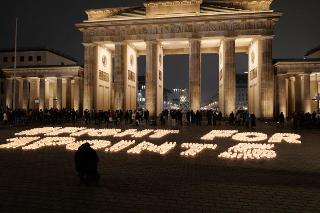 Eine Gruppe von Menschen steht vor dem beleuchteten Reichstag in Berlin, Deutschland, umgeben von Geb├Ąuden, Masten und L├Ąmpchen; 'Kampf für Freiheit' ist auf dem Boden im Vordergrund geschrieben.