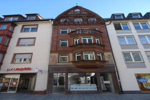 Ein Geschäftsgebäude mit zahlreichen Fenstern, das sich an einer Straße in Heidelberg, Deutschland, unter einem klaren blauen Himmel befindet.