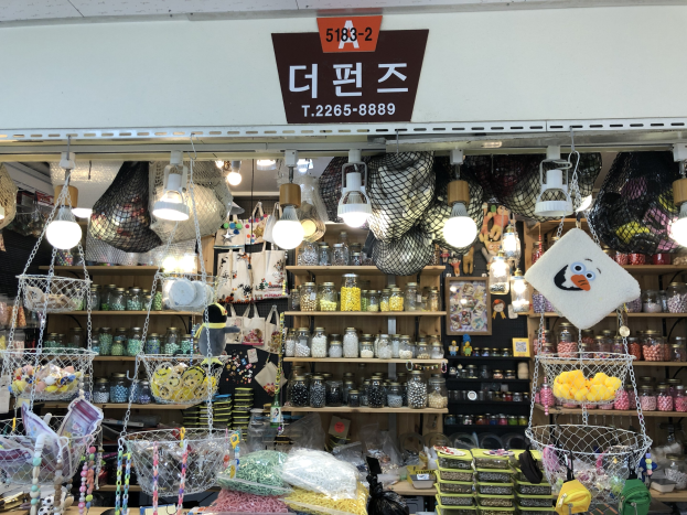 Ein unordentlicher Laden in Seoul, der verschiedene Gegenstände wie Körbe, Lichter, Flaschen und Spielzeuge auf Regalen ausstellt, mit einer Tafel öber dem Eingang, die darauf hinweist, dass es sich um den besten koreanischen Shop handelt.