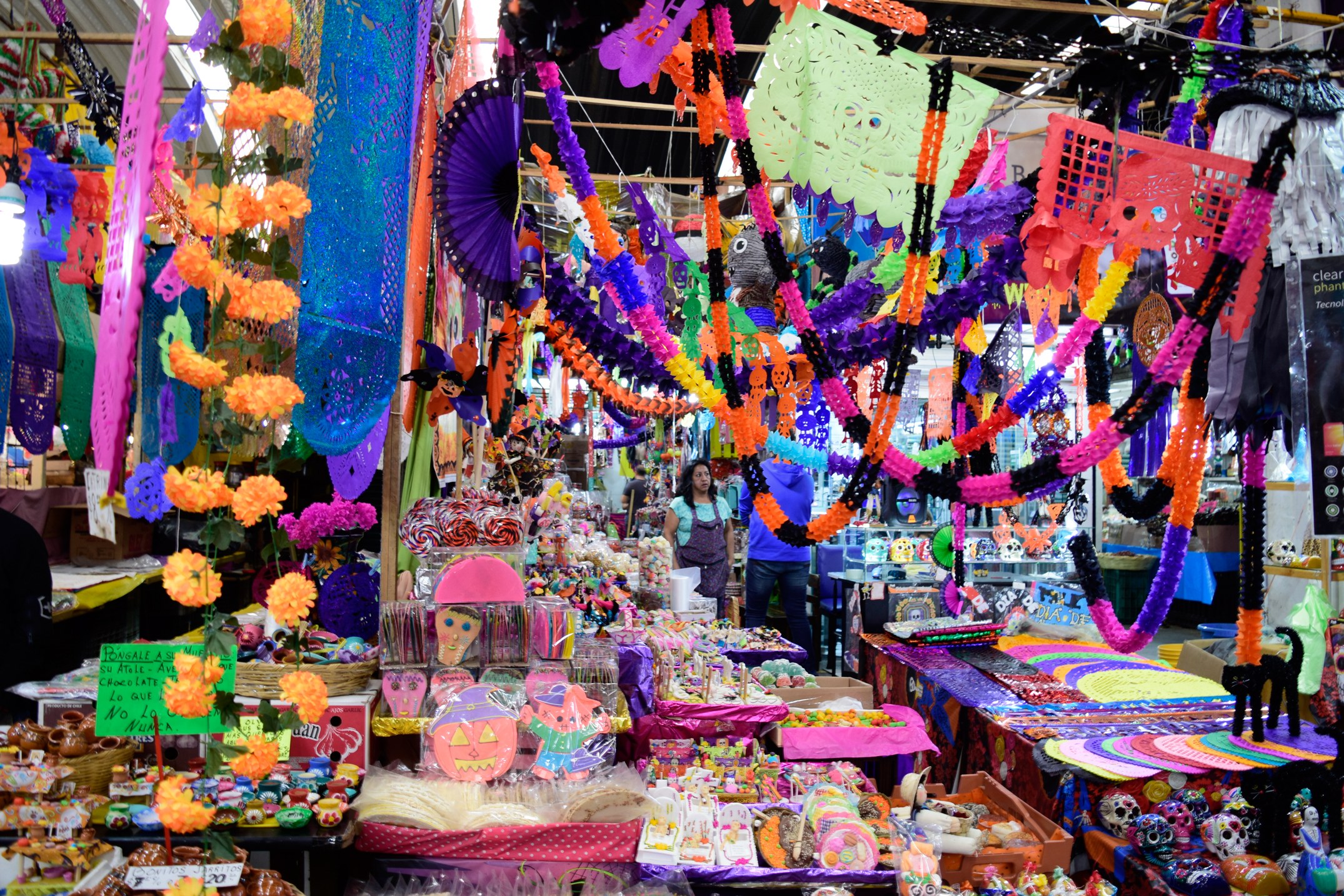 Ein belebter Markt mit Ständen, die Spielzeug, Dekorationsgegenstände und andere Gegenstände verkaufen, Menschen, die durch die Gänge schlendern, und Deckenbeleuchtung.