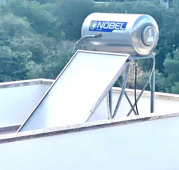 Solarwassererwärmer mit einem auf einem Gebäude installierten Speicher, Bäume im Hintergrund.