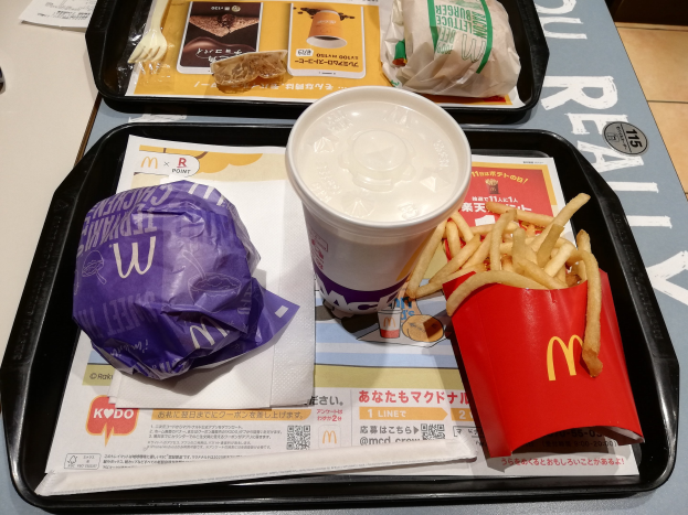 Ein Tisch mit einem Tablett, das einen McDonald's-Essen aus French Fries, einem Kaffee, einem Papier, einer Gabel, einem Messer und anderen Gegenständen enthält.