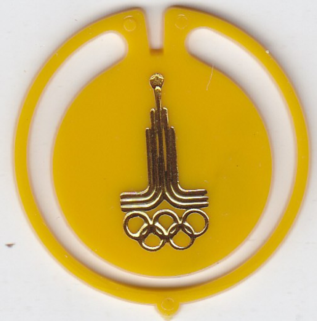 Olympisches Ringe-Abzeichen mit einem goldenen Logo in der Mitte auf einem gelben kreisförmigen Abzeichen vor einem weißen Hintergrund.