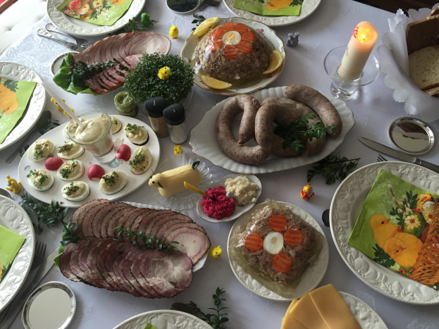 Ein langer Tisch mit verschiedenen Gerichten, Geschirr, Gläsern und Kerzen, umgeben von Stühlen, was auf ein traditionelles deutsches Osteressen hinweist.