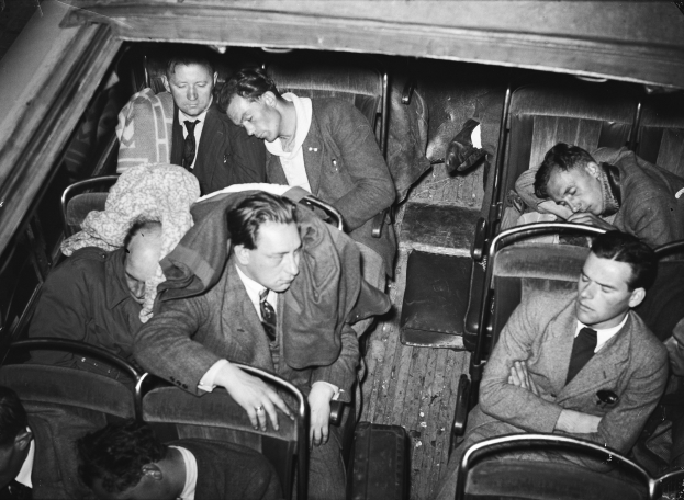 Ein Schwarz-Weiß-Bild einer Gruppe von Männern in Anzügen, die auf einem Bus sitzen.