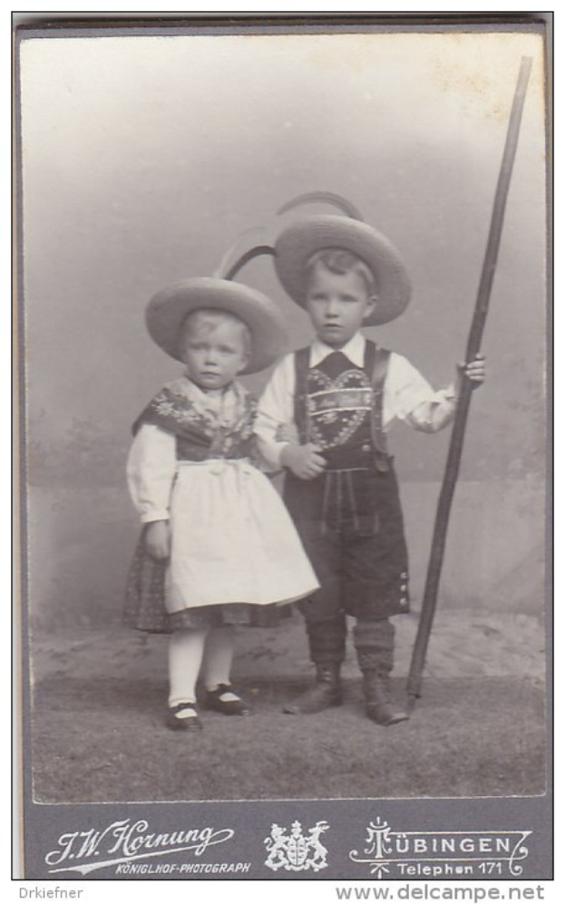 Schwarzes und weißes Foto von zwei Kindern in traditioneller bayerischer Tracht, eines hält einen Stock, mit Text unten.
