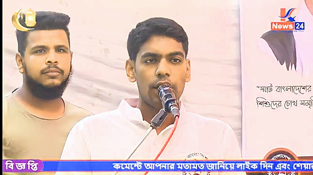 Zwei Männer stehen nebeneinander vor einem Fernseher, einer spricht in ein Mikrofon, der andere trägt ein graues T-Shirt und steht vor einer Banner mit Text und Logo.