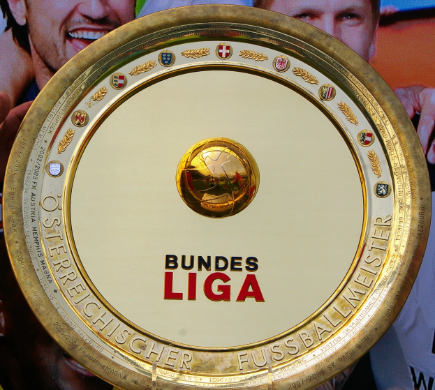 Goldener Schild mit "Bundesliga"-Text in der Hand eines Mannes, im Hintergrund ein Banner mit drei Personen