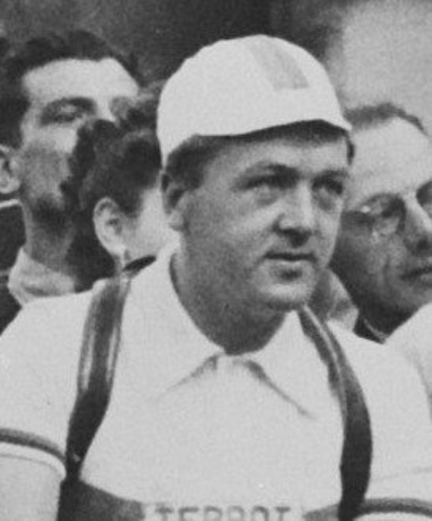 Schwarzes und weiße Foto eines Mannes mit Mütze und Hosenträgern vor einer Gruppe von Menschen, der legendären Füttballspieler.